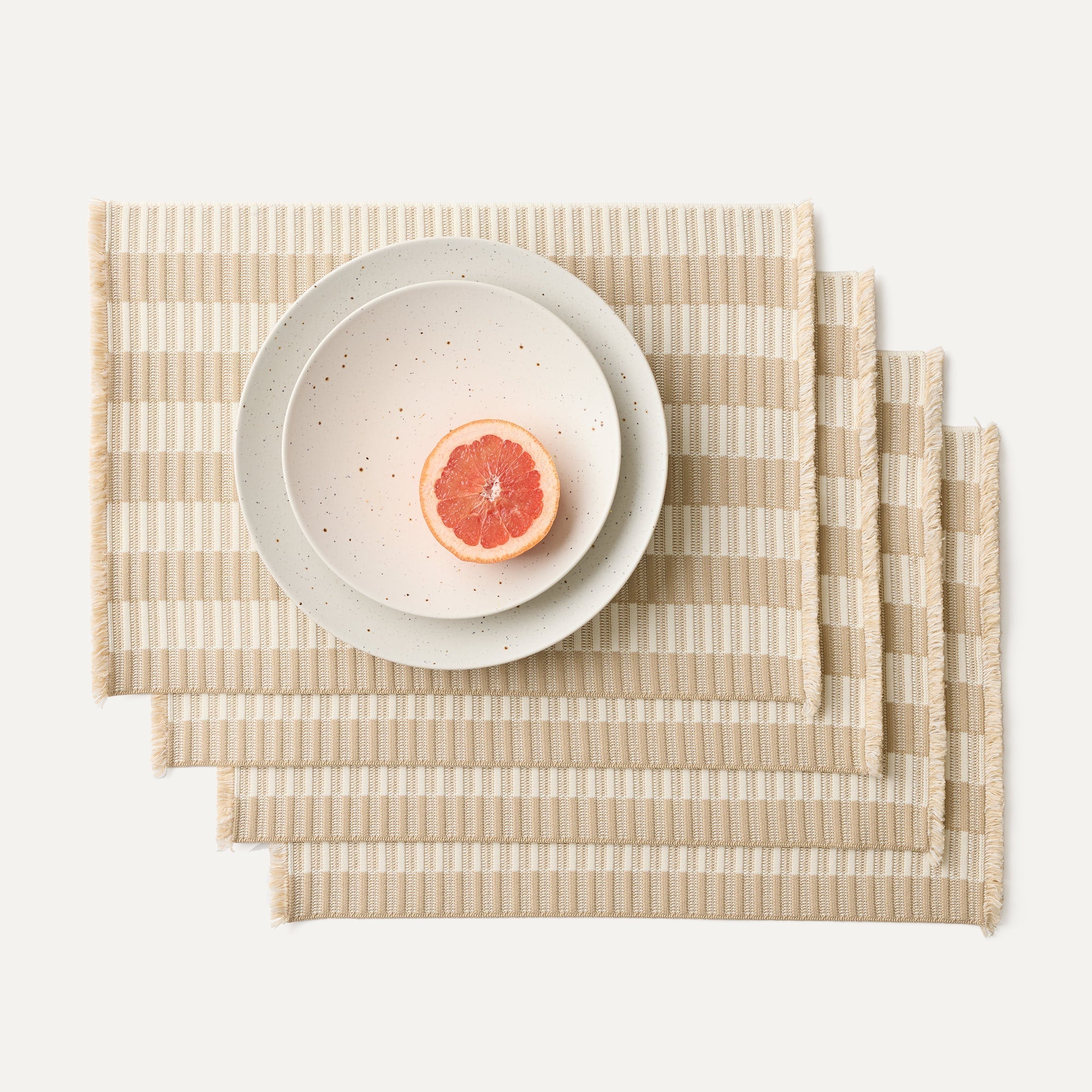 A set of four Placemats in Almond Fringe shown with a plate setting.